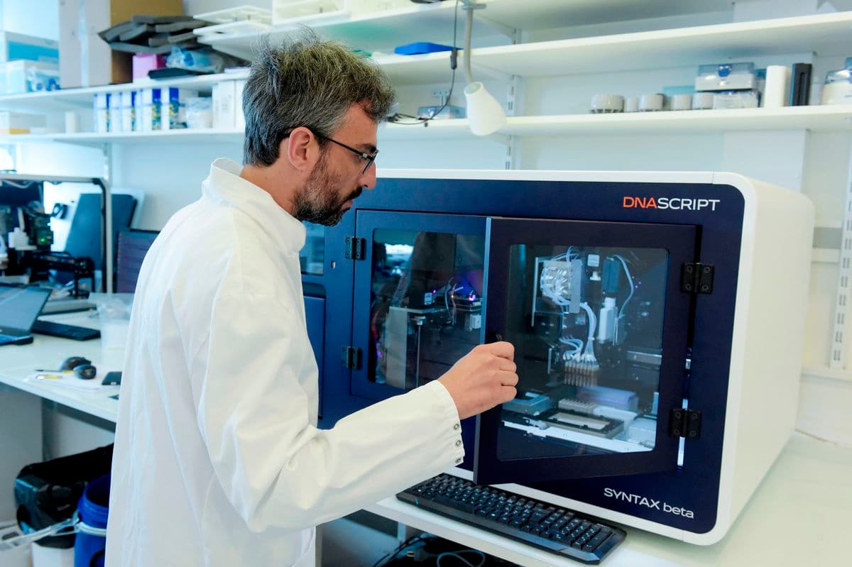 白衣を着た男性が実験器具を扱っている。背景の棚には備品や科学機器が並んでいる。